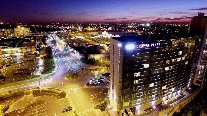 a cityscape with a tall building illuminated by the crowne plaza logo , and a busy street filled with cars at Crowne Plaza Dublin - Blanchardstown