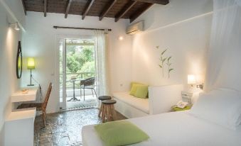 a white bedroom with a bed , a couch , and a tv . the room has a balcony overlooking the garden at Skiathos Holidays Suites & Villas