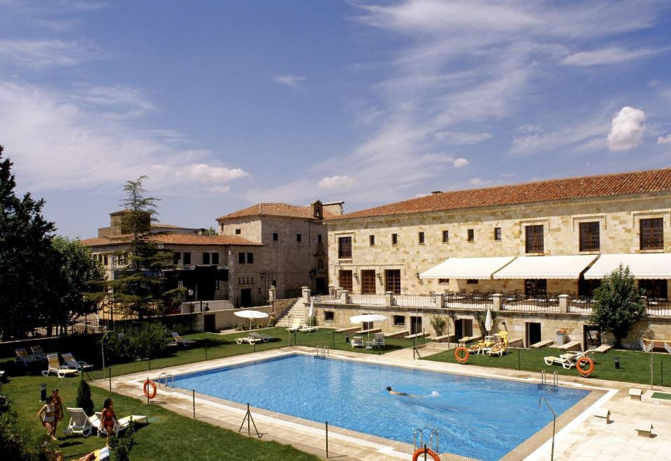 a large swimming pool is surrounded by a stone building and has people in the water at Parador de Zamora