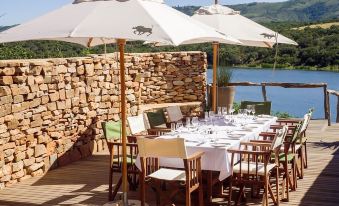 an outdoor dining area with a long table set for a meal , surrounded by umbrellas and chairs at Pumba Private Game Reserve