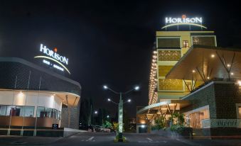"a large hotel building with its name "" horizon "" on top , surrounded by other buildings and trees at night" at Horison Gkb Gresik