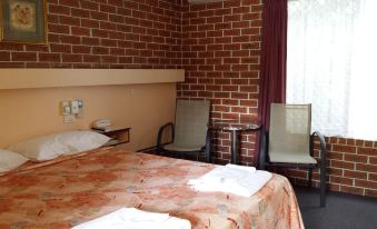 a hotel room with a double bed , two chairs , and a brick wall behind the bed at The Mullum Motel