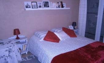a bedroom with a bed , red blanket , and white bedding , along with a bookshelf above the bed at Les Bambous