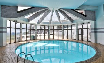 a large , round pool is surrounded by a glass - enclosed patio and sits under a skylight at Hotel Home Green Home