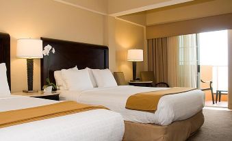 a large bed with white linens and a brown headboard is in a room with two lamps at Best Western Oceanfront