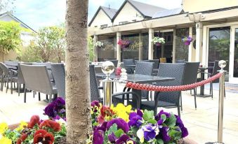 an outdoor dining area with tables and chairs , surrounded by potted plants and flowers , in front of a building at Horse & Hound