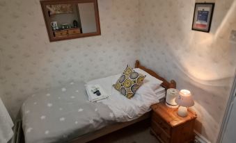 a bed with a white sheet and pillow is placed next to a small table with a lamp at The Village Inn