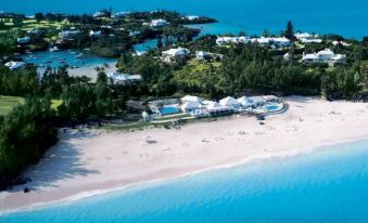 aerial view of a sandy beach with a large house on the shore and several people enjoying themselves in the water at Rosewood Bermuda