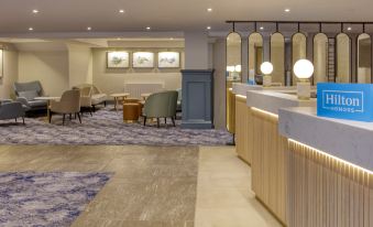 a hotel lobby with a reception desk , chairs , and a chandelier , creating a warm and inviting atmosphere at Hilton Cobham
