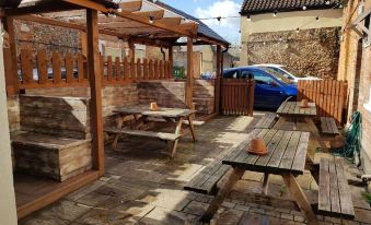 a wooden patio area with benches , tables , and chairs under a pergola , as well as a car parked nearby at The Westgate