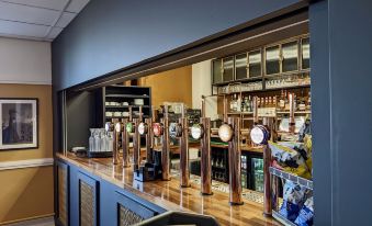 a bar with multiple beer taps and a large window showing the outside of the establishment at The Beaches Hotel