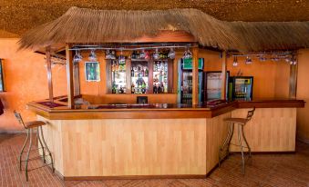 a bar with a thatched roof , surrounded by various bottles of alcohol on display for sale at Belvedere Hotel