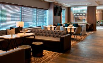 a modern lounge area with brown leather couches , chairs , and tables , as well as a bar in the background at Marriott Boston Quincy
