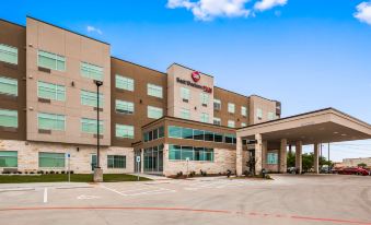 a large , modern hotel building with a red sign on the front and a parking lot in front at Best Western Plus Executive Residency Austin