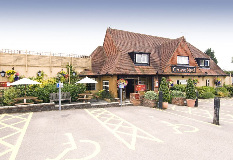 a brick building with a thatched roof , surrounded by bushes and trees , under a clear blue sky at Premier Inn Tring