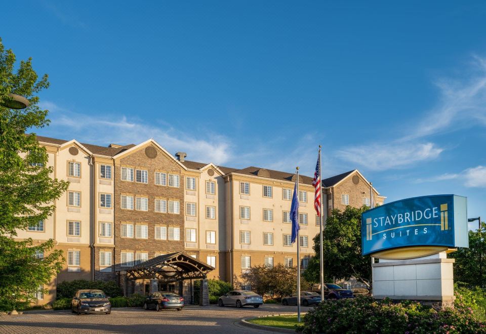 "a large hotel with a sign that says "" staybridge suites "" and flags flying in front of it" at Staybridge Suites Milwaukee Airport South