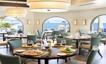 a restaurant with round tables and chairs , a view of the ocean through the windows at Oyster Bay Beach Resort