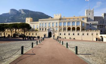 a grand palace with a large white building and a red brick pathway leading up to it , surrounded by people at Riviera Marriott Hotel la Porte de Monaco