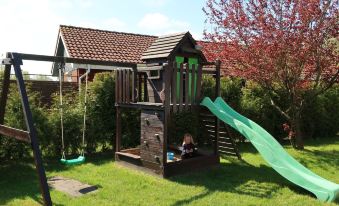 a wooden playhouse with a slide is set up in a grassy area near a tree and house at Martin