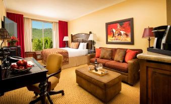 a hotel room with a large bed , a couch , a desk , and a chair , all situated near a window overlooking the outdoors at The Lodge at Jackson Hole