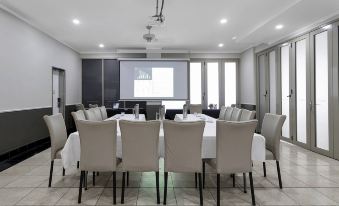 a conference room with a large table surrounded by chairs and a projector screen on the wall at Mantra Mackay