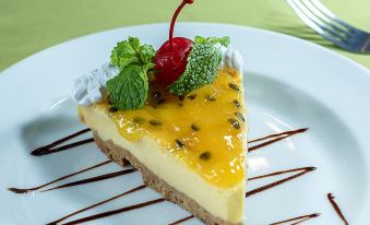 a slice of cheesecake with a cherry on top and a mint leaf on top , served on a white plate at Hotel Playa Bejuco