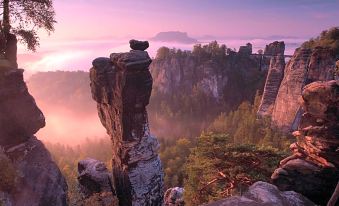 a picturesque view of a mountain range with a large rock formation in the foreground at Berghotel Bastei