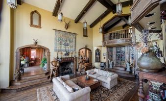 a spacious living room with wooden beams , a large chandelier , and multiple couches and chairs arranged around a fireplace at Highlands Castle Overlooking Lake George Plus 2 Other Castles & Suites
