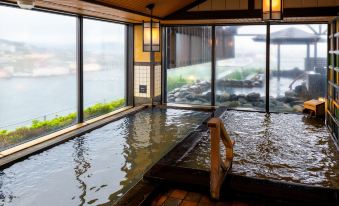 a modern japanese - style room with large windows offering a view of the surrounding landscape , and a wooden - floored hot spring bathtub filled with at La Vista Hakodate Bay