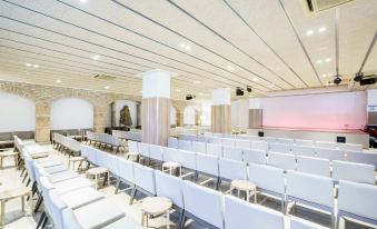 a large conference room with rows of white chairs arranged in front of a projector screen at Estival Park Silmar