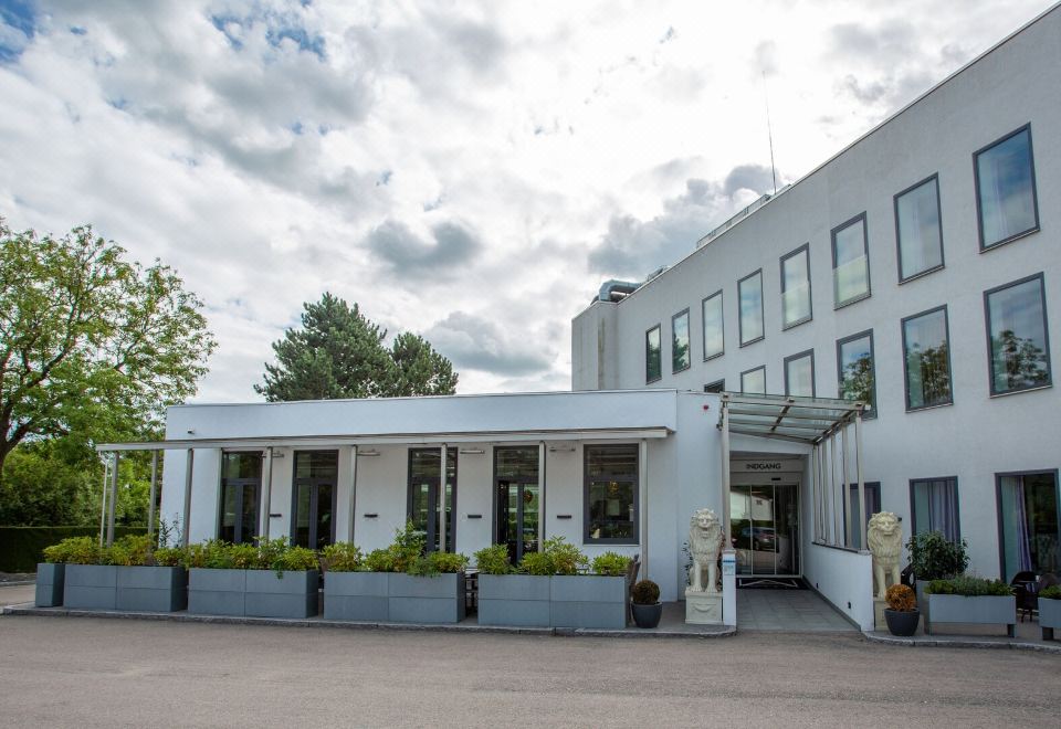 a white building with a porch and potted plants in front of it , under a cloudy sky at A Hotels Glostrup