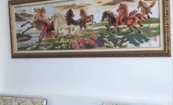 a framed tapestry with horses running in a field and people sitting on a couch at Hotel Nguyen Ngoc