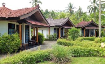 a row of small wooden houses surrounded by a lush green lawn , with trees in the background at Tasik Ria Resort