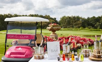 a table with a variety of drinks and food is set up next to a golf cart in front of a floral display at Forest of Arden Country Club