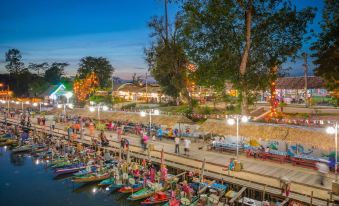 a bustling night market scene with numerous people gathered around boats docked on the river at Sakol Hotel