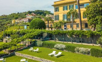 a large yellow building with a garden area in front , surrounded by greenery and white chairs at Villa Riviera Resort