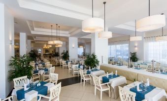 a large , well - lit restaurant with white and blue dining tables , chairs , and potted plants , creating a welcoming atmosphere for guests at Bahia Principe Grand la Romana - All Inclusive