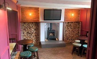 a cozy living room with a fireplace , wooden tables , and stools , as well as a television mounted on the wall at The White Horse