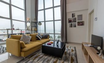 The modern space features a living room with a yellow couch and a large window that offers a view of the beachfront area at JK Maritime Luxury Suite
