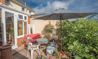 a backyard with a red couch , patio set , and an umbrella , surrounded by potted plants and flowers at Clarendon