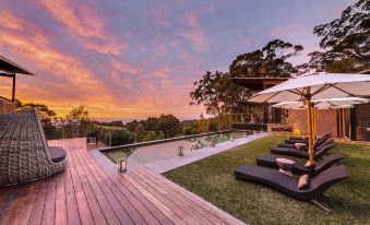 a beautiful outdoor area with a pool , sun loungers , and umbrellas , as the sun sets in the background at Spicers Sangoma Retreat