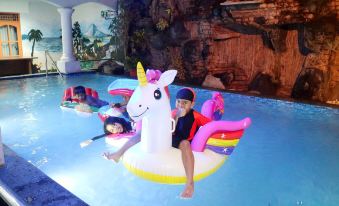 a group of children , including a boy and a girl , are playing on an inflatable unicorn float in a swimming pool at Mason Residence Syariah Ciawi