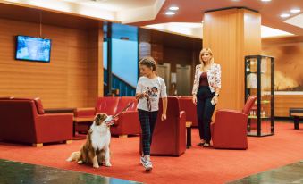 a woman and a girl are walking a brown and white dog on a leash in a hotel lobby at Hotel Kompas