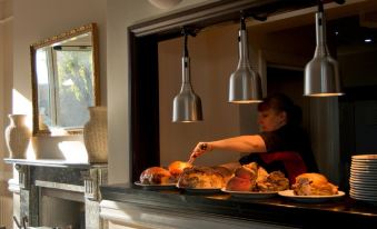 a woman wearing a black apron is standing in a restaurant , preparing food on a table at Crofts Hotel