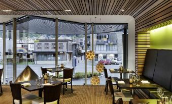 a modern restaurant with wooden ceiling and glass doors , featuring a dining area with tables and chairs at Novotel Queenstown Lakeside