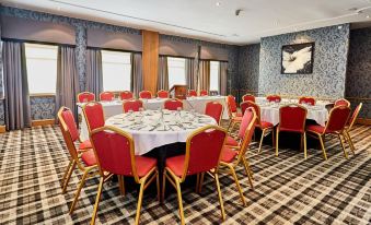 a large conference room with multiple round tables , chairs , and a television mounted on the wall at Abbotsford Hotel