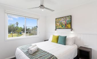 a white bedroom with a large bed , a ceiling fan , and a window overlooking the street at Ingenia Holidays Lake Conjola