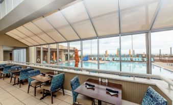 a restaurant with a large window overlooking a pool and city skyline , featuring blue chairs and tables at DoubleTree Suites by Hilton Melbourne Beach Oceanfront