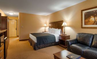 a hotel room with a bed , couch , nightstand , and lamps , as well as a leather chair and a tv at Grand Hotel at Bridgeport