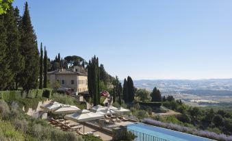 a large villa with a pool and a view of the surrounding landscape , set against a clear blue sky at Rosewood Castiglion del Bosco